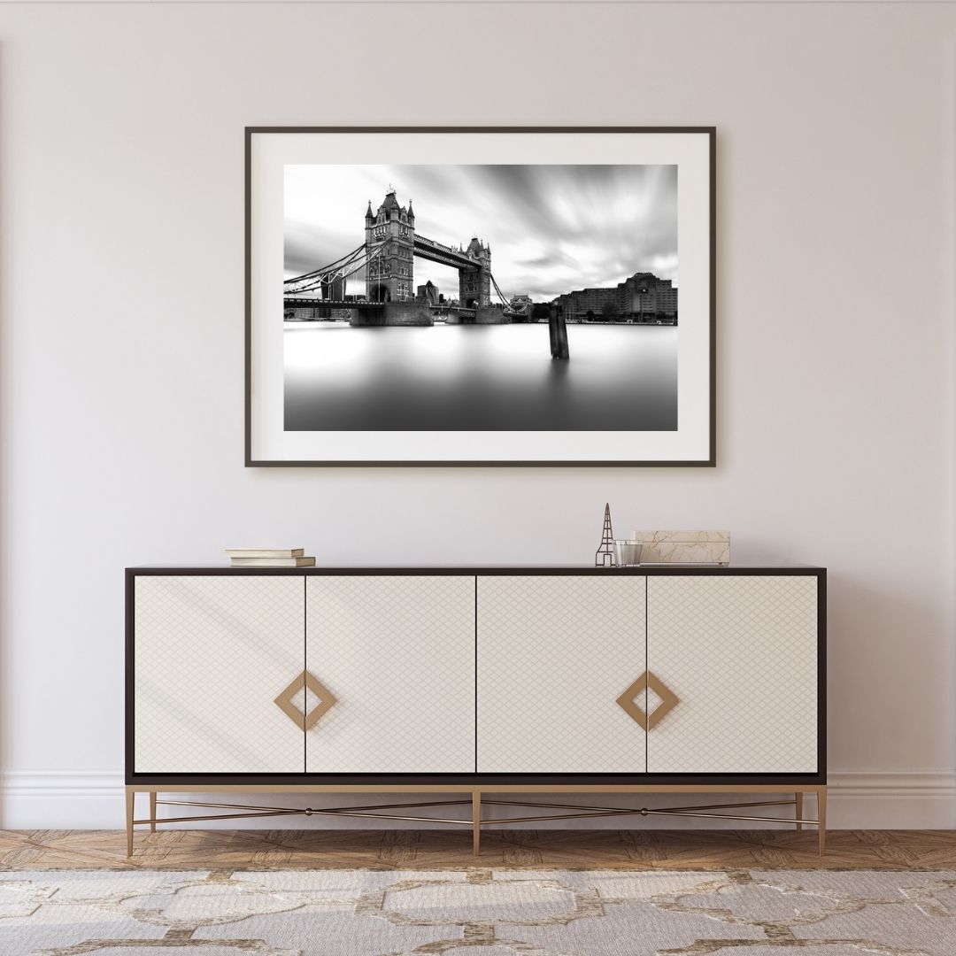 Framed black and white photograph of a bridge above water on a wall above a decorative cabinet.