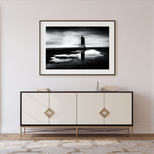 Framed black and white artwork of a lighthouse on a wall above a decorative cabinet.
