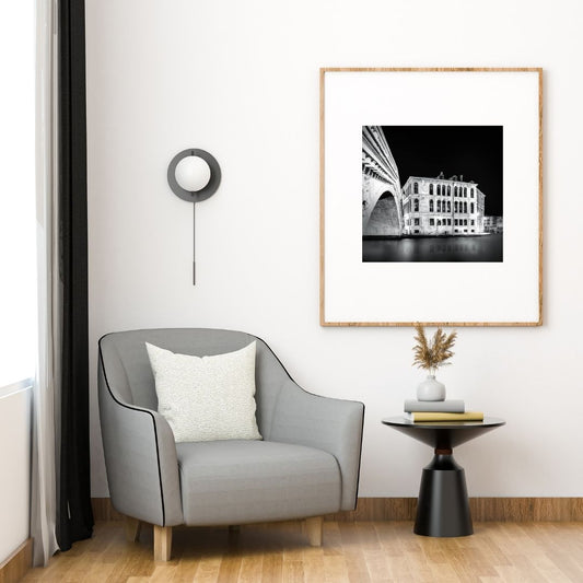 Modern living room with a gray armchair, side table, and framed artwork on the wall.