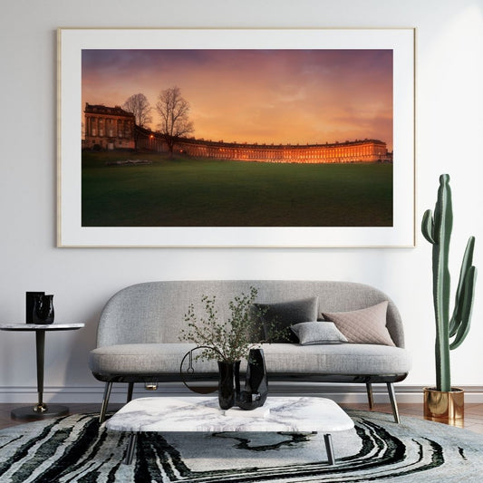 Living room with a large framed photograph of a sunset over a building, a gray sofa, and decorative items.