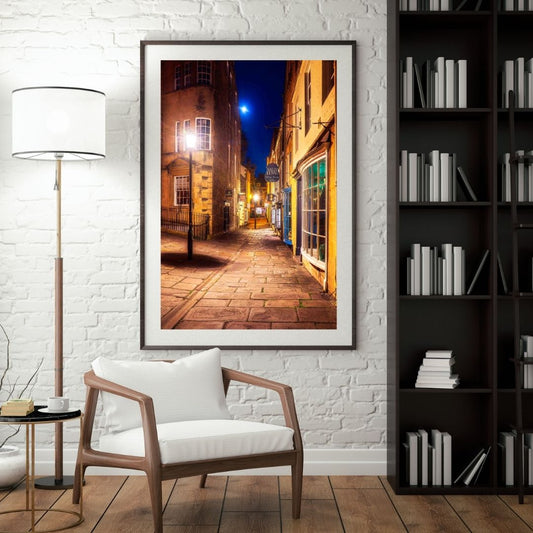 Framed photograph of a street scene on a white brick wall above a wooden chair.