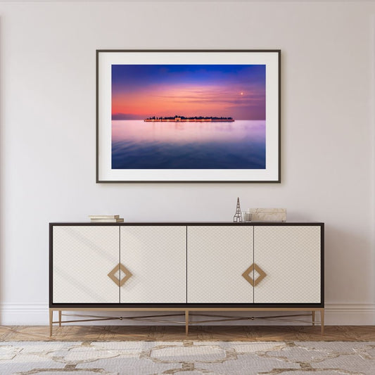 Framed artwork of San Michele at sunset over water above a decorative cabinet.