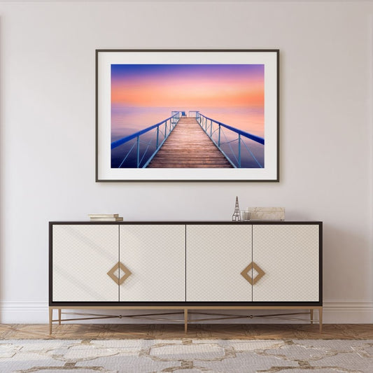 Framed artwork of a sunset over a dock above a decorative cabinet.