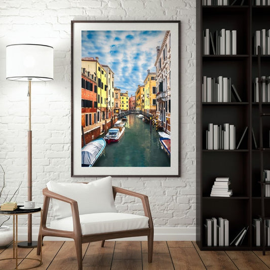Framed artwork of a canal scene in a living room with a chair and lamp.