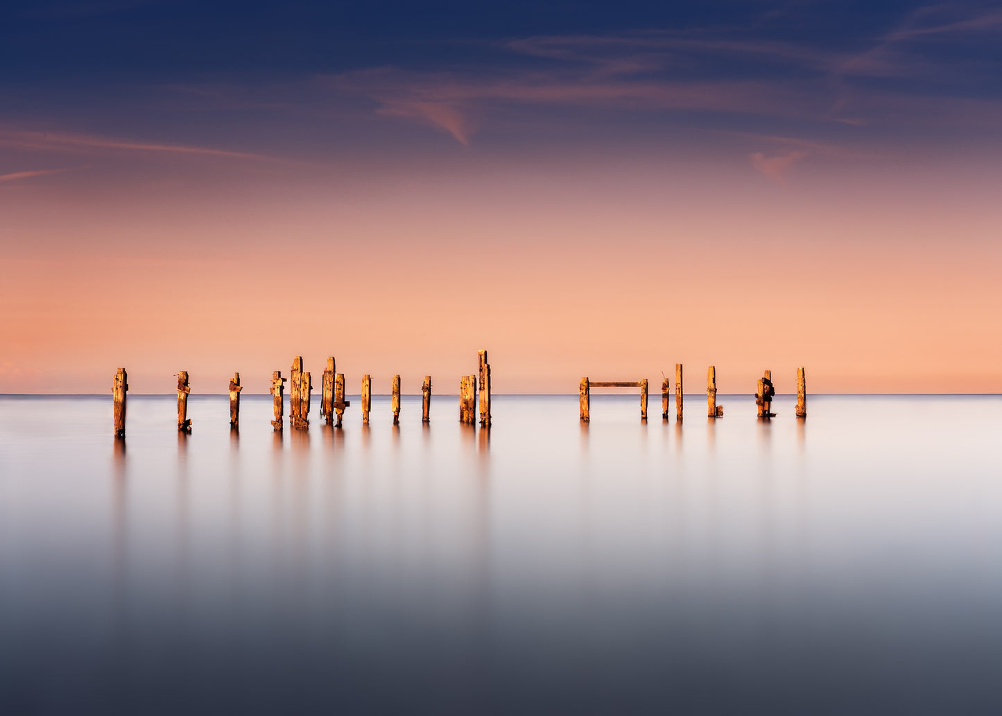 Minimalist seascape of Swanage’s old pier, weathered wooden posts against soft peach and blue evening sky.