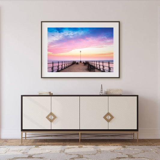 Framed artwork of a sunset over a pier above a decorative cabinet.