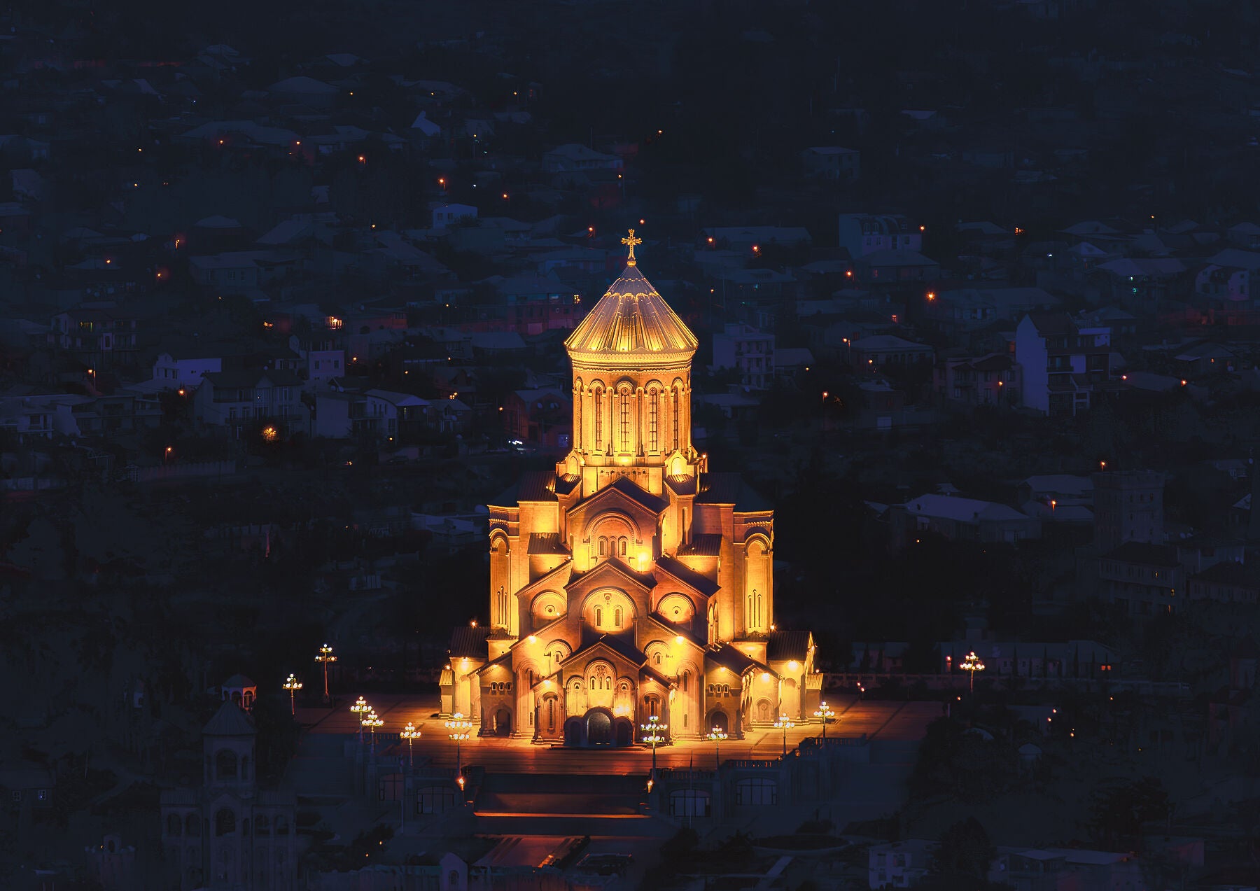 Golden-lit Sameba Cathedral in Tbilisi, Georgia, glowing at night against the dark city skyline.