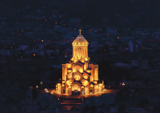 Golden-lit Sameba Cathedral in Tbilisi, Georgia, glowing at night against the dark city skyline.