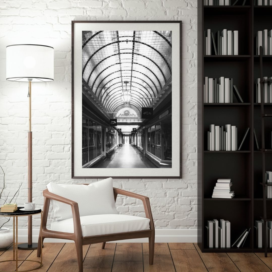 Framed black and white photo of a train station archway in a living room setting with a chair, lamp, and bookshelf.