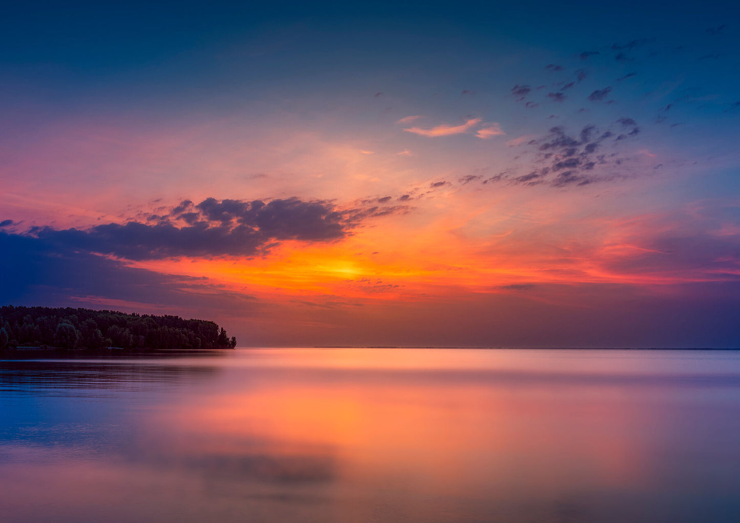 Sunrise over the Dnipro River near Kyiv, with warm sky colors reflected in calm water and a silhouetted shoreline