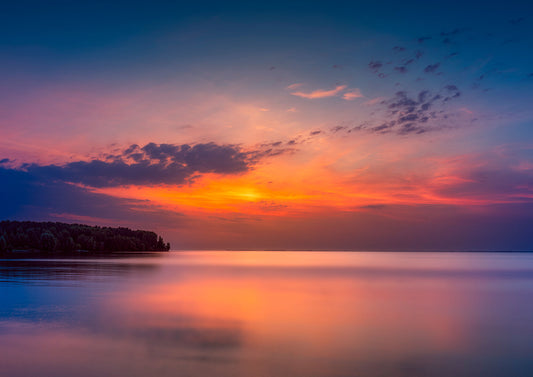 Sunrise over the Dnipro River near Kyiv, with warm sky colors reflected in calm water and a silhouetted shoreline