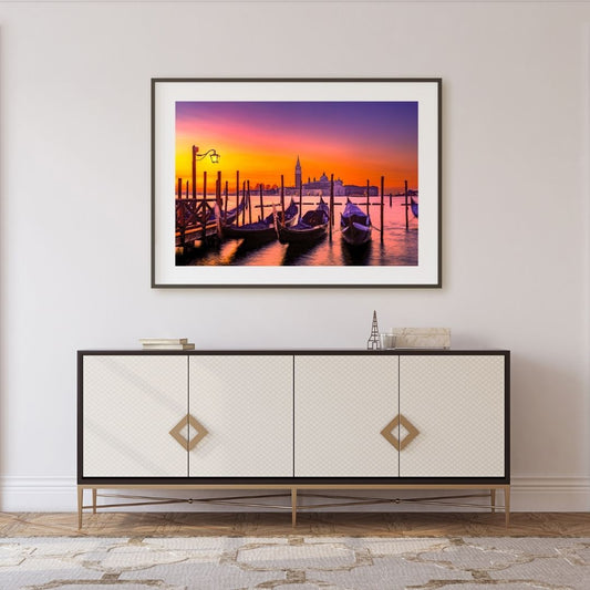 Framed artwork of a sunset over a dock with gondolas, displayed above a decorative cabinet.