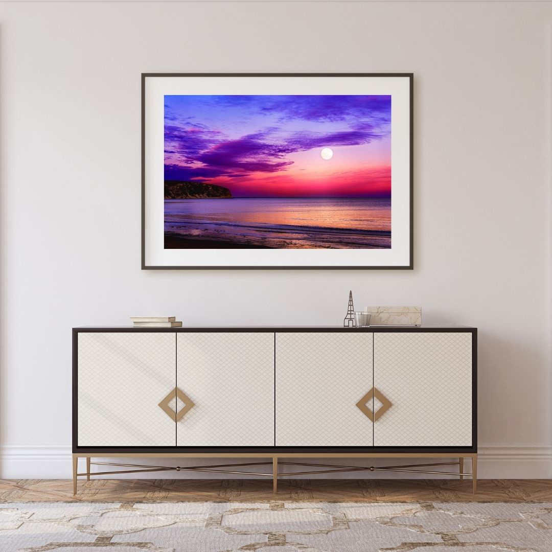 Framed artwork of a sunset over water above a decorative cabinet.