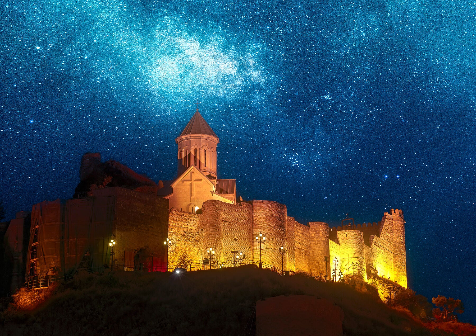 Illuminated Narikala Fortress and church glowing under a vibrant star-filled sky in Tbilisi, Georgia