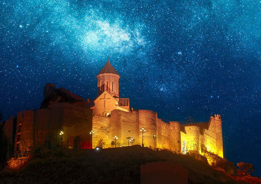 Illuminated Narikala Fortress and church glowing under a vibrant star-filled sky in Tbilisi, Georgia