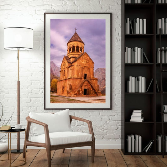 Framed photograph of a church on a wall in a room with a chair, lamp, and bookshelf.