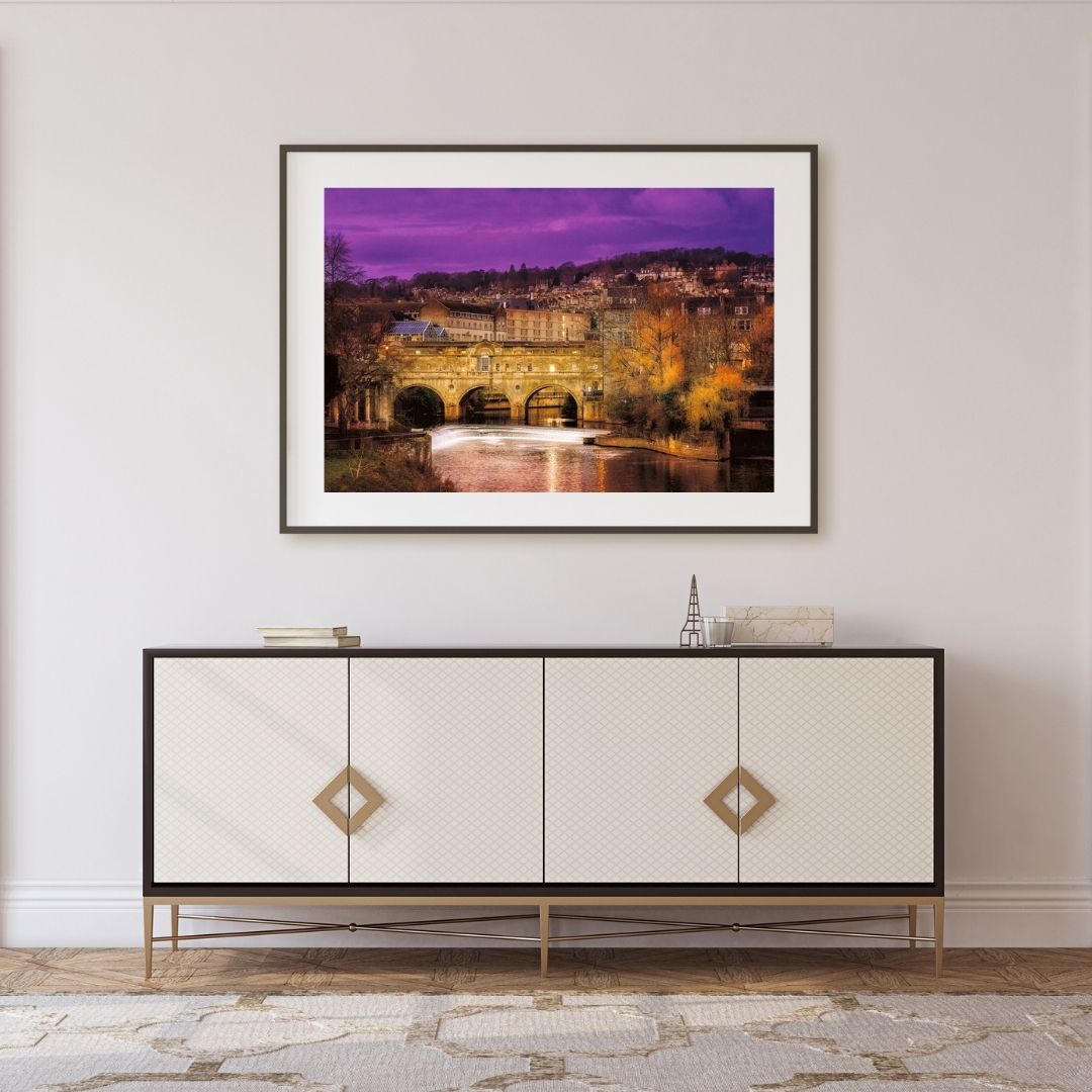 Framed artwork above a decorative cabinet in a room with a purple sky.