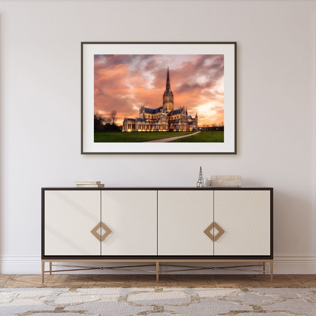 Framed photograph of a sunset over Salisbury Cathedral on a wall above a decorative cabinet.