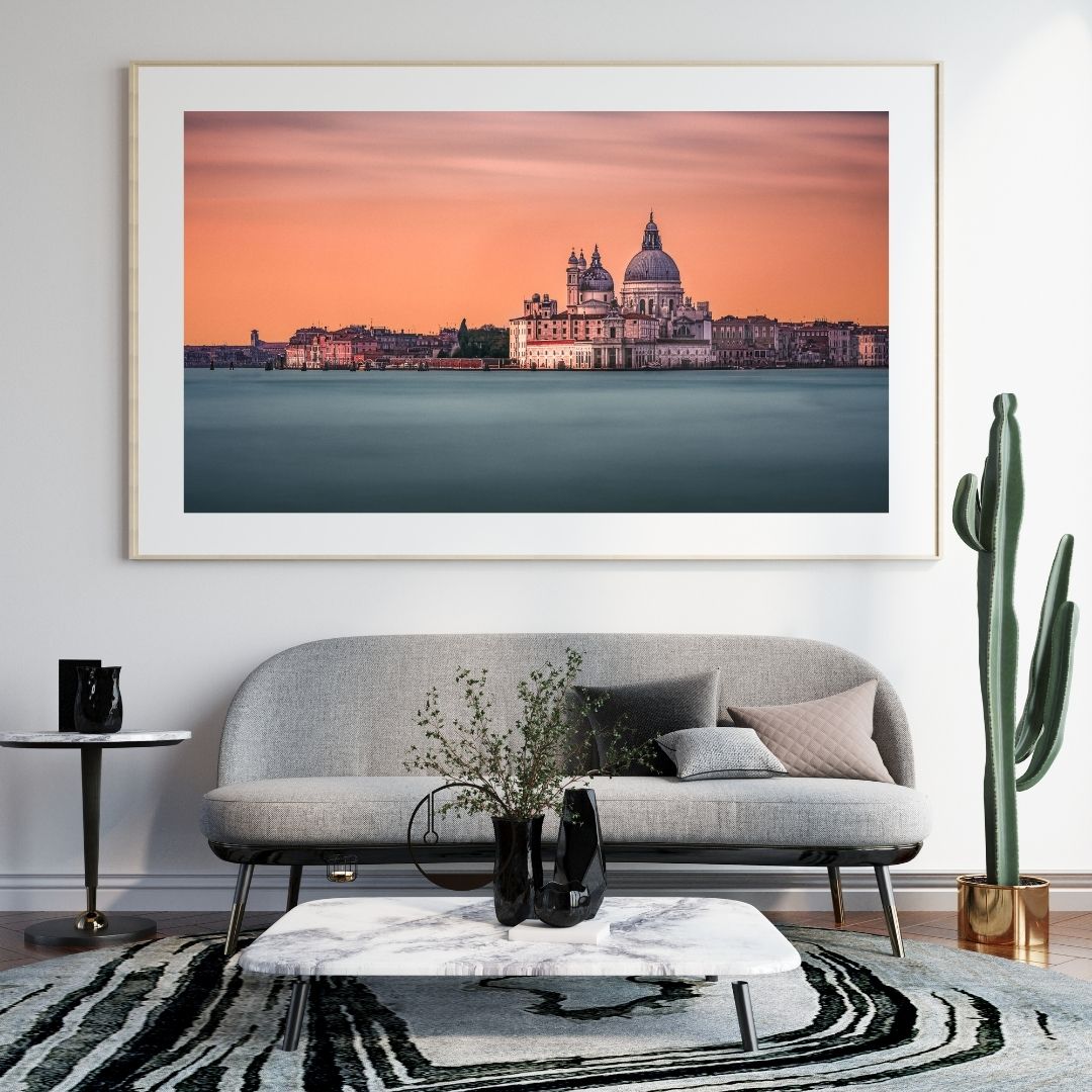Framed artwork of a cityscape with a sunset over water, displayed above a gray sofa in a living room.