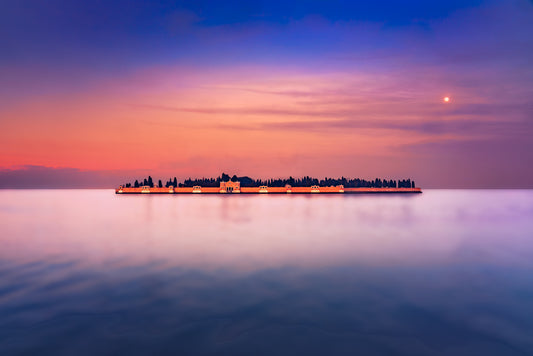 San Michele cemetery island in Venice glowing at dusk, with a serene moonlit sky and smooth lagoon waters, fine art photograph by John Wright.