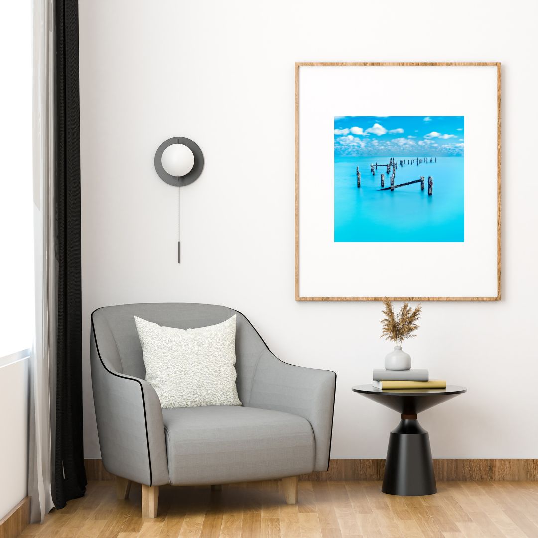 Modern living room with a gray armchair, side table, and framed artwork of a dock.