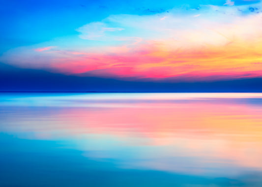 Long-exposure photograph of sunrise over the Dorset coast, with vivid blue, pink, and gold clouds reflected on calm sea water.