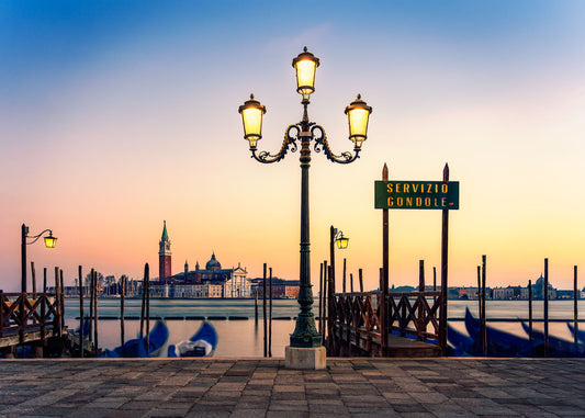 Fine art photograph of a Venetian street lamp glowing at sunrise with San Giorgio Maggiore and gondolas on the Grand Canal