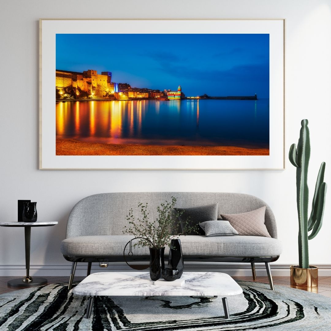 Framed artwork of a coastal cityscape above a gray sofa in a living room.