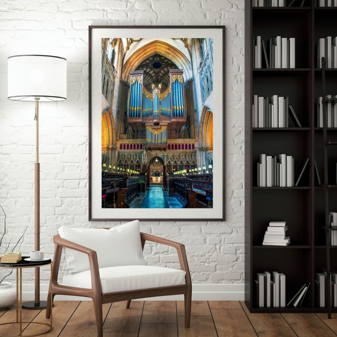 Framed picture of a cathedral interior on a wall above a wooden chair with white cushions.