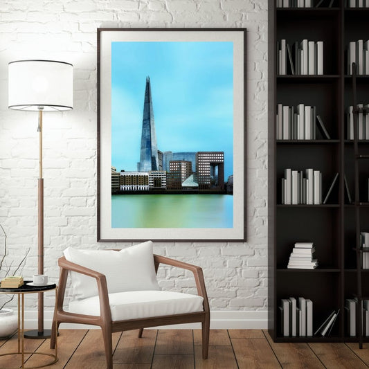 Framed cityscape print on a wall above a wooden chair in a room with a lamp and bookshelf.