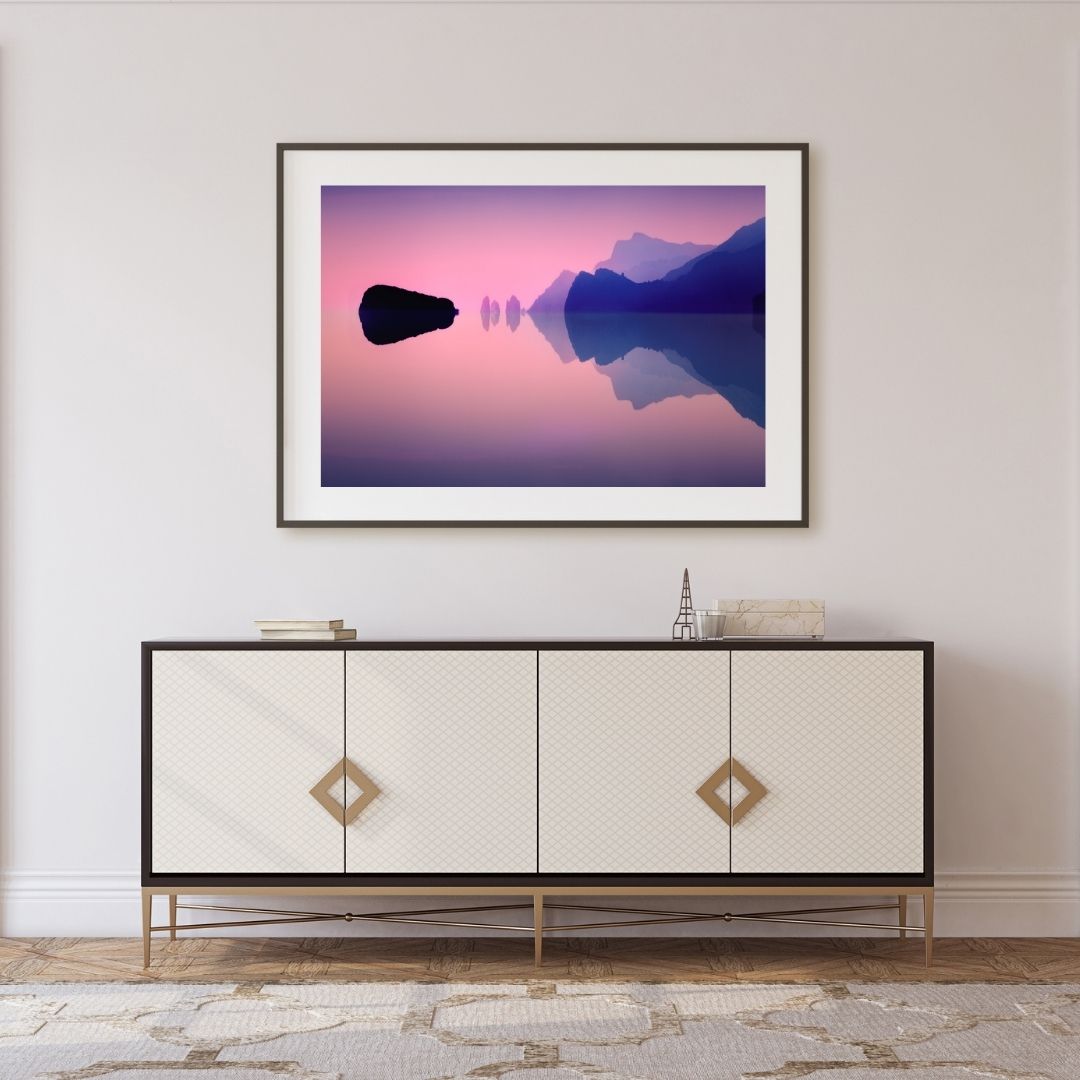 Framed artwork of a mountain landscape above a decorative cabinet.