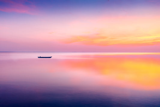 Fine art seascape photograph of a lone boat on calm water beneath a radiant sunrise with pastel pink, orange, and lavender tones.