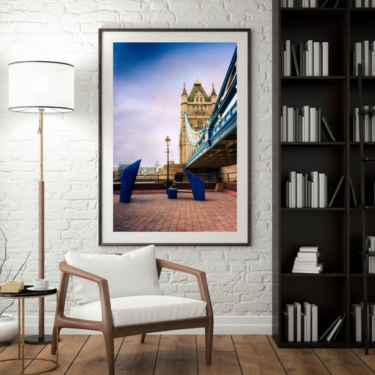 Framed photograph of a cityscape with a bridge on a white brick wall above a wooden chair.