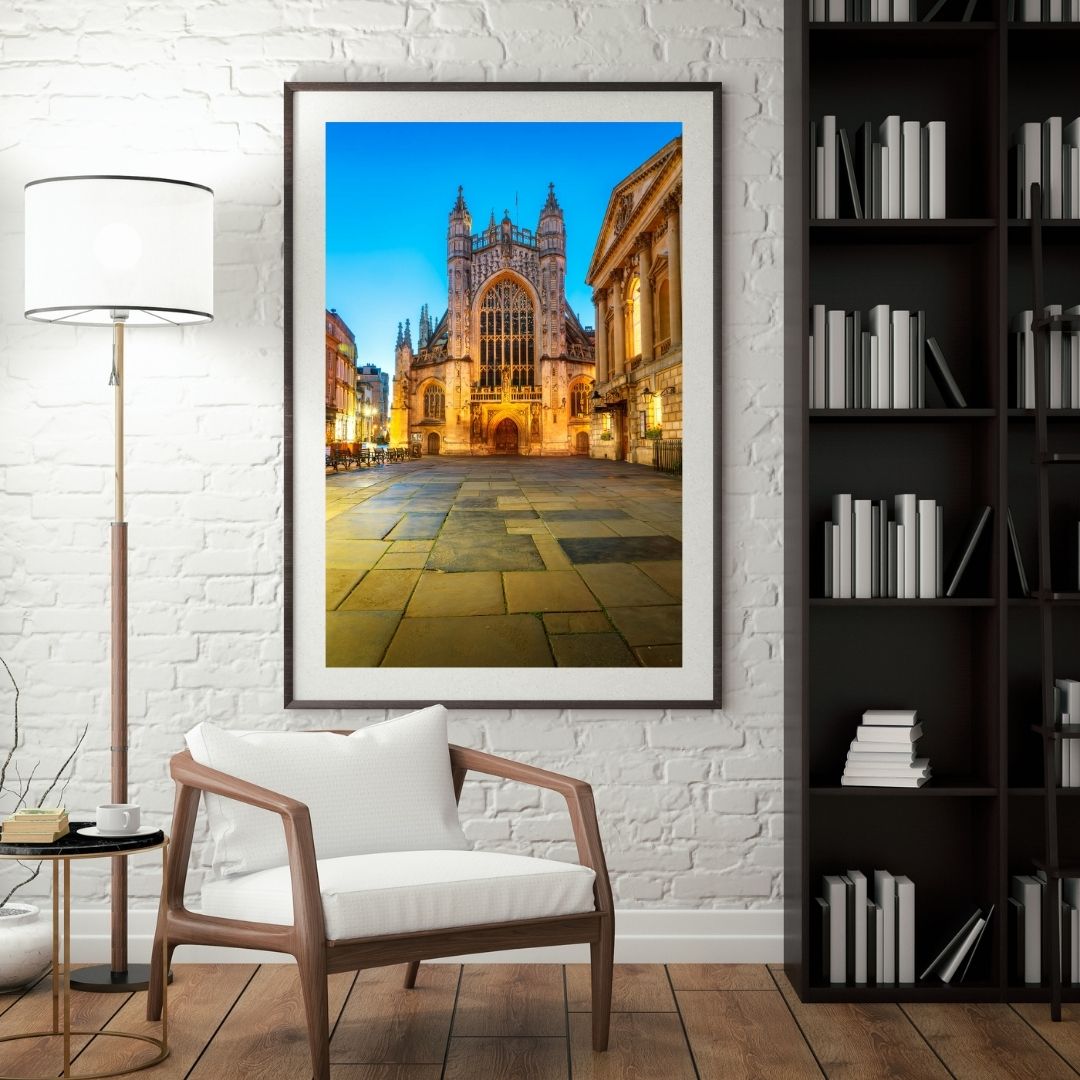 Framed photograph of a cathedral on a wall in a room with a chair, lamp, and bookshelf.