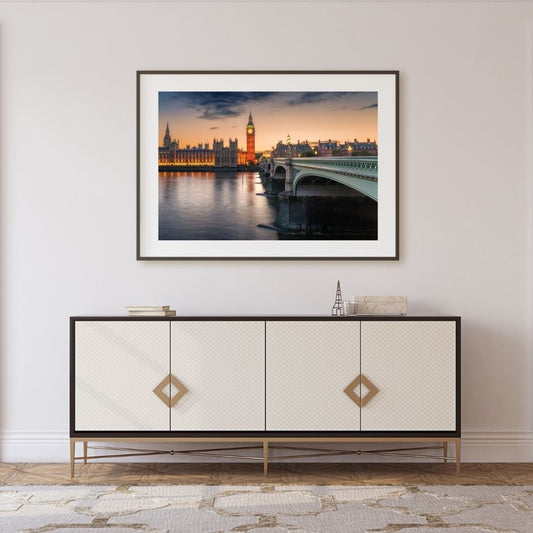 Framed artwork of a cityscape with a bridge and clock tower, displayed above a decorative cabinet.