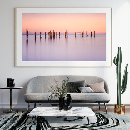 Framed artwork of a sunset over water with a gray sofa and decorative items in a living room.