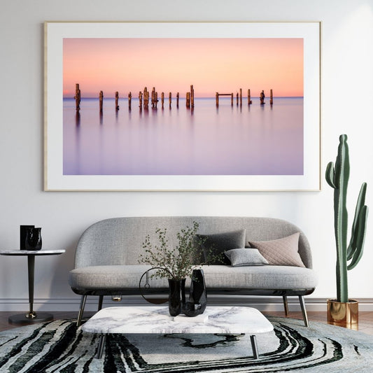 Framed artwork of a sunset over water with a gray sofa and decorative items in a living room.