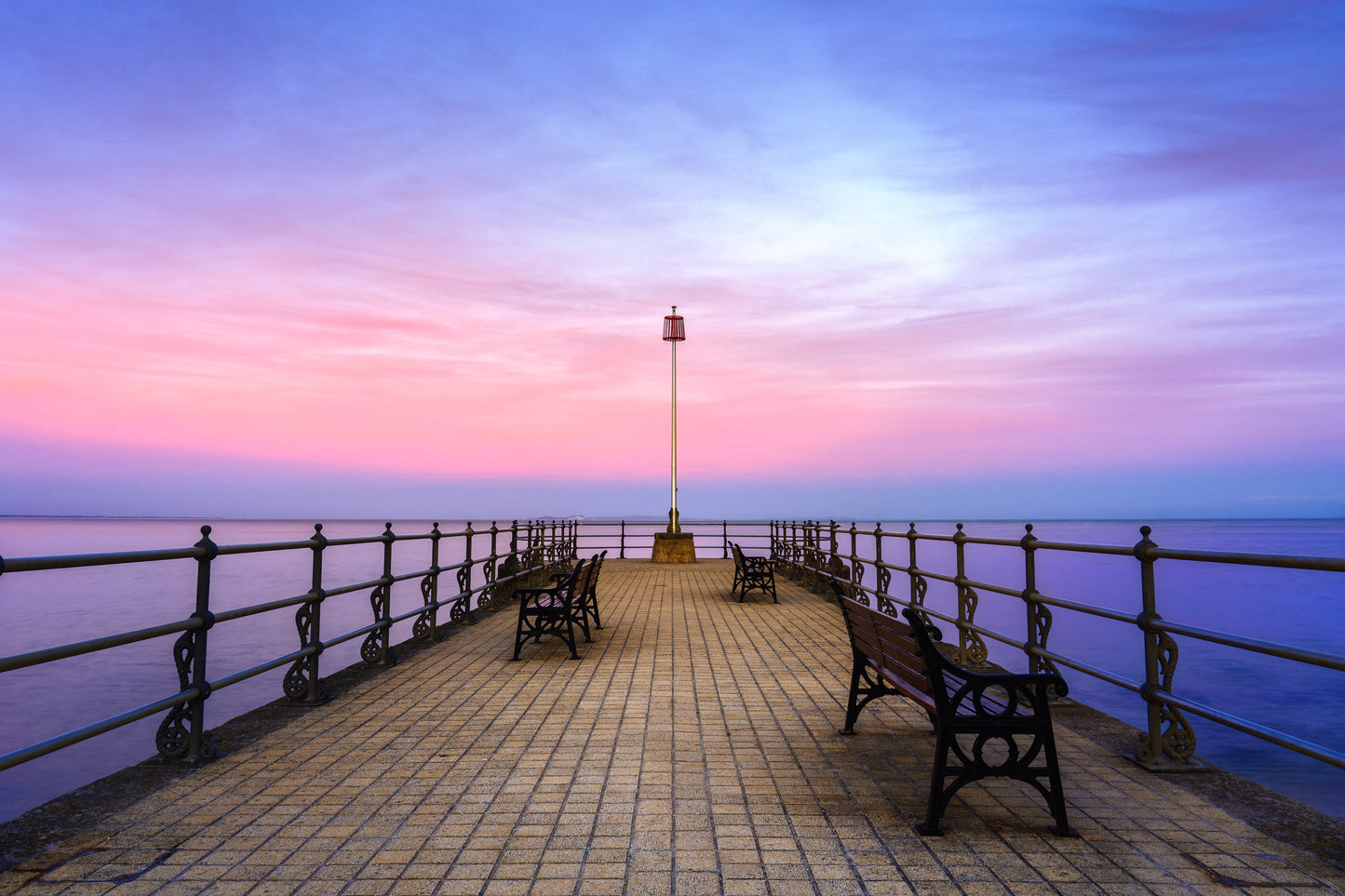 Banjo Pier in Swanage at twilight with benches, calm sea, pastel sky, and a supermoon rising beyond the horizon.