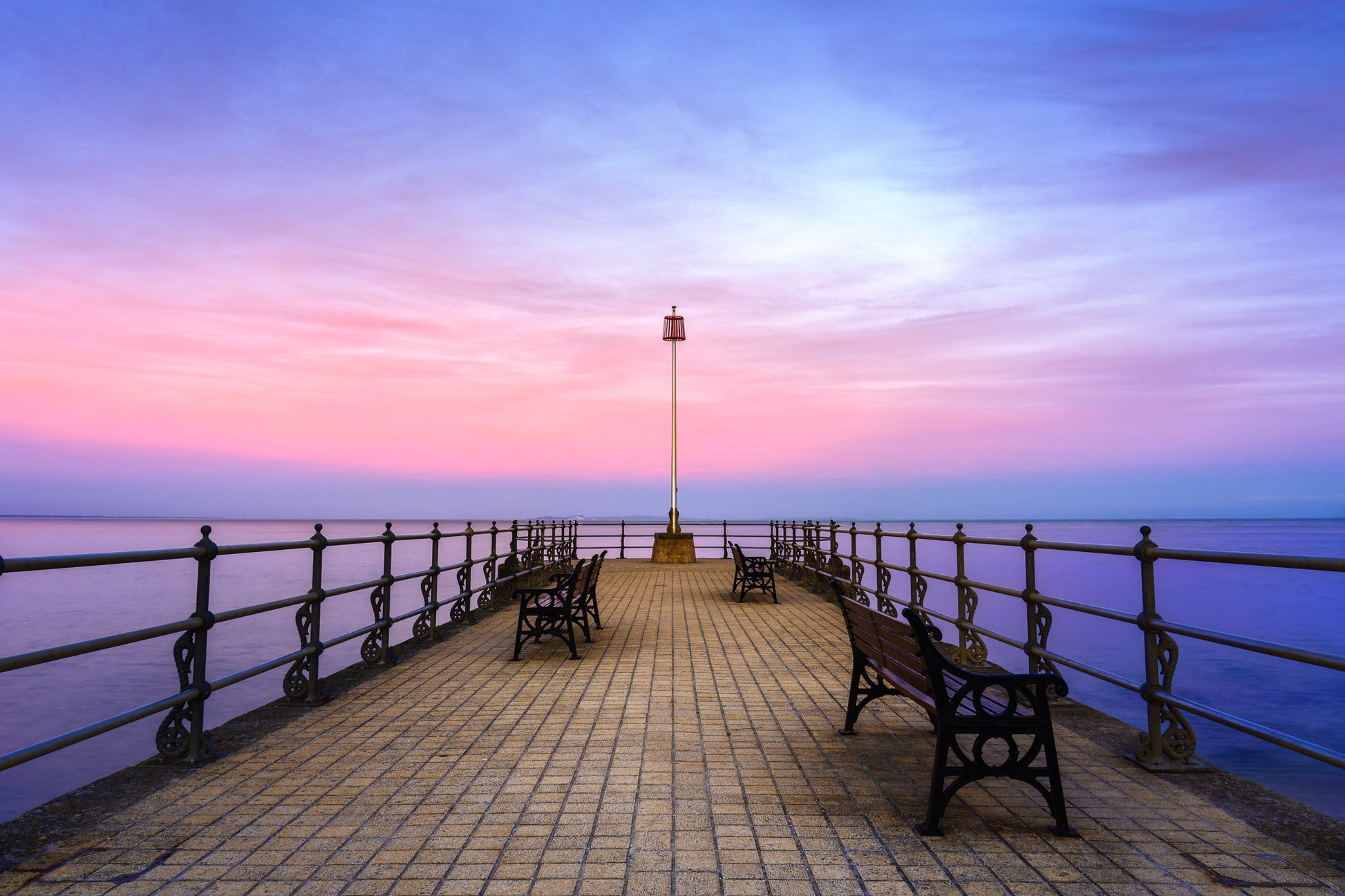 Banjo Pier in Swanage at twilight with benches, calm sea, pastel sky, and a supermoon rising beyond the horizon.