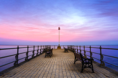 Banjo Pier in Swanage at twilight with benches, calm sea, pastel sky, and a supermoon rising beyond the horizon.