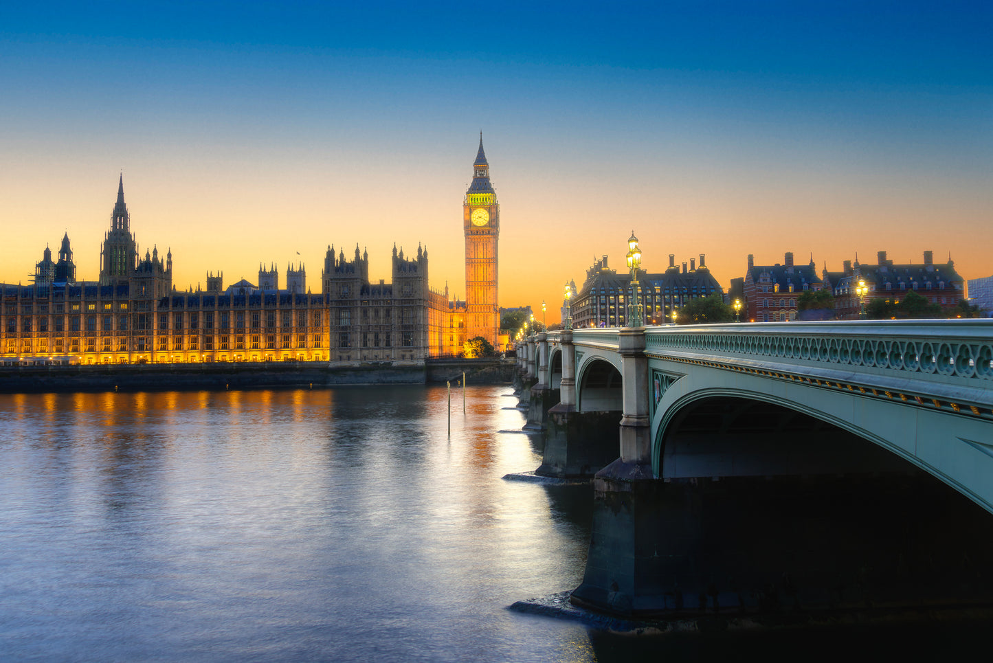 Big Ben and the Houses of Parliament at sunset with Westminster Bridge and soft reflections on the River Thames.
