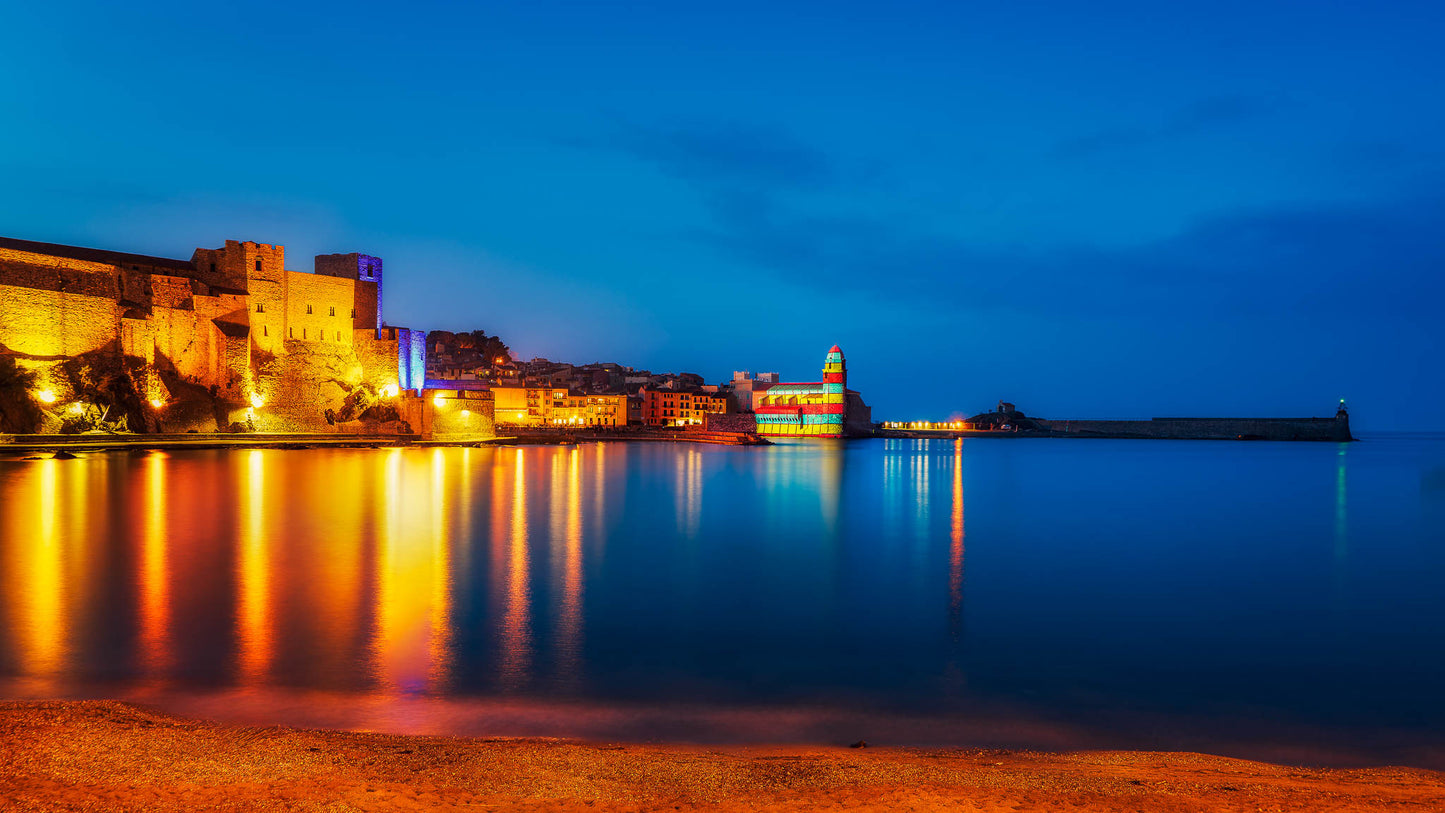 A fine art photograph of Collioure, France, showing golden reflections across the harbour and deep blue evening water after sunset.