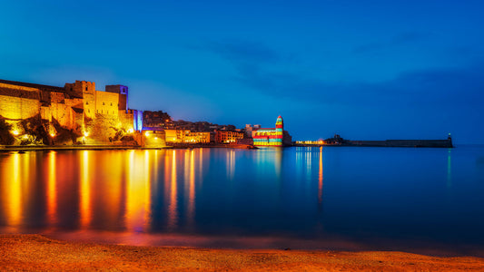 A fine art photograph of Collioure, France, showing golden reflections across the harbour and deep blue evening water after sunset.
