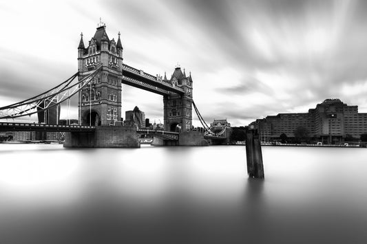 Black and white long-exposure photograph of Tower Bridge in London, with smooth water and streaking clouds, by fine art photographer John Wright.