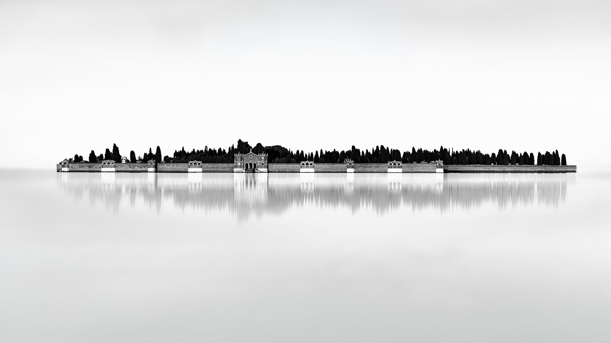 Black and white minimalist photograph of San Michele cemetery island in Venice, reflected in still water with architectural detail and cypress trees.