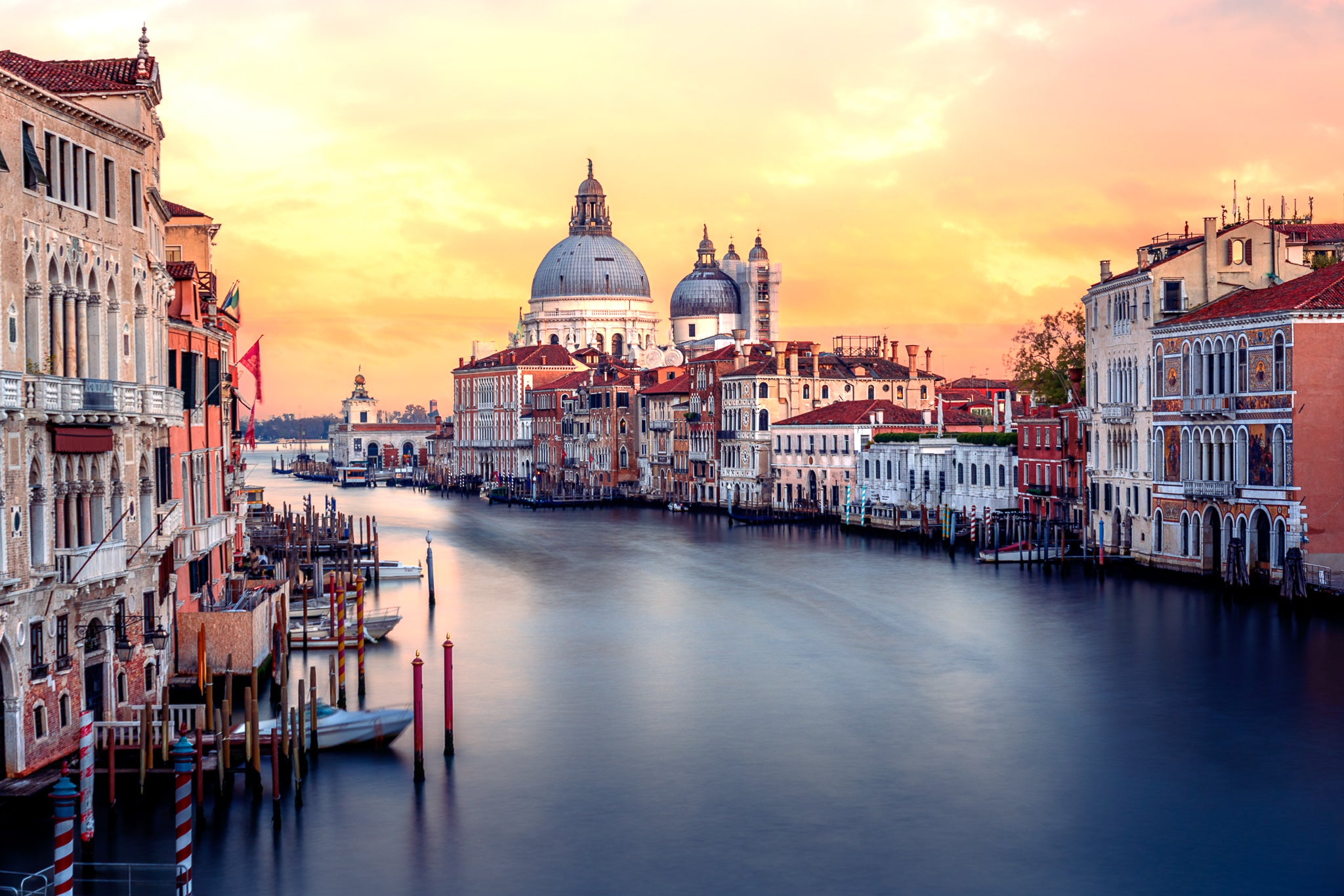 Colour photograph of the Grand Canal in Venice at sunset with Santa Maria della Salute and historic buildings reflected in calm water