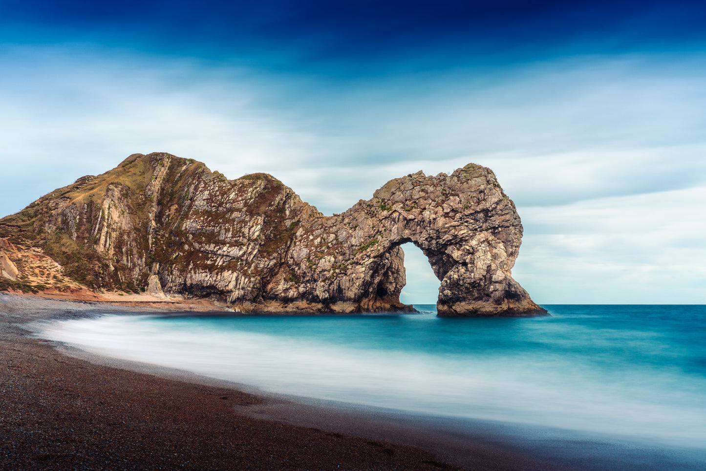 Fine art seascape photograph of Durdle Door in Dorset, showing the limestone arch with smooth water and sky in autumn light.