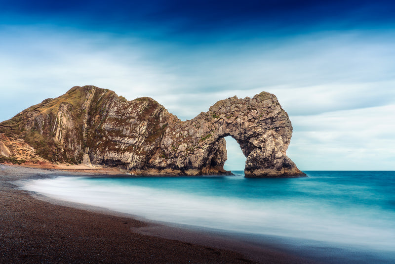 Fine art seascape photograph of Durdle Door in Dorset, showing the limestone arch with smooth water and sky in autumn light.