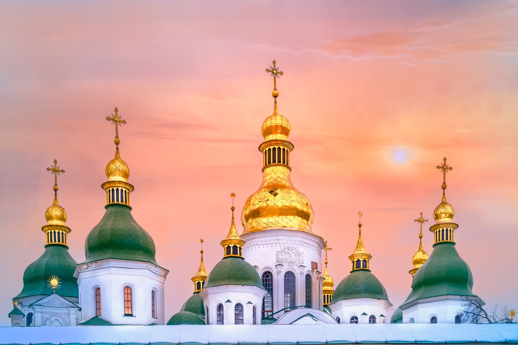 Colour photograph of Saint Sophia Cathedral in Kyiv with golden domes and green spires illuminated by warm sunset light