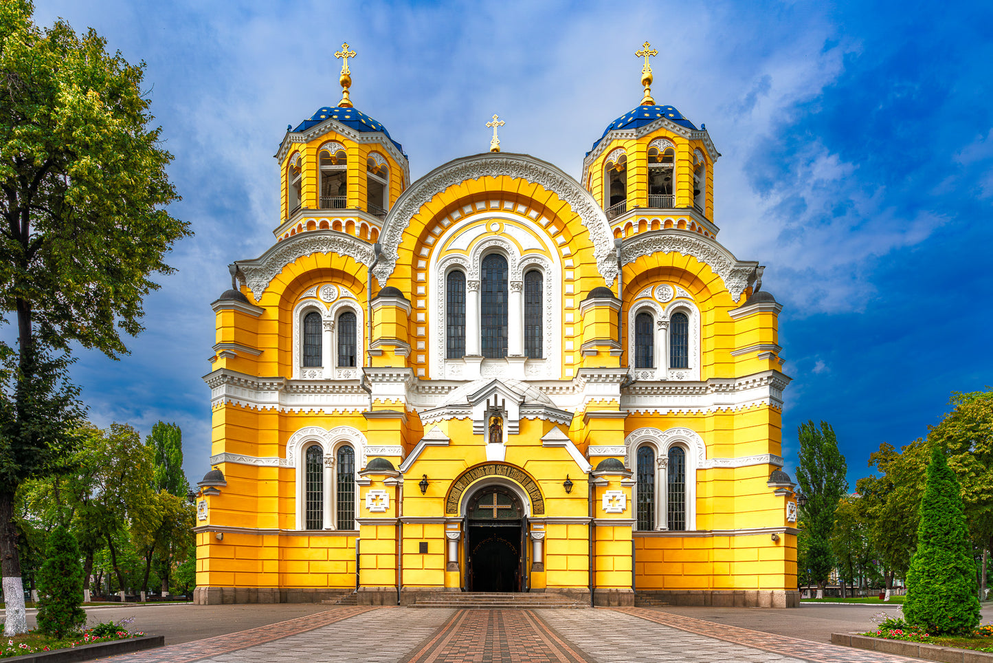 Colour photograph of Saint Volodymyr’s Cathedral in Kyiv with a bright yellow facade and blue domes beneath a clear sky